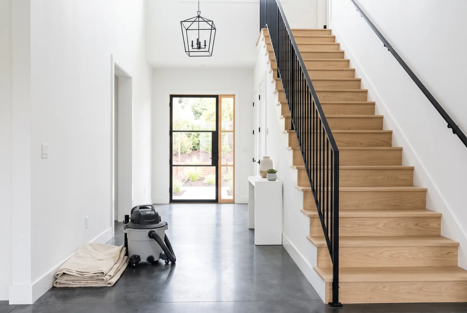 Newly built home entryway with clean white oak stairs, a black railing and a glass front door after a post-construction clean
